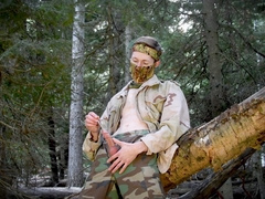 Soldier sounding his strung up bone in the wilderness near a fallen tree.
