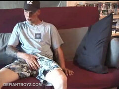 Young amateur Brandon reclines on the sofa and pulls off his pants. Watching porn video, he rubs his dick hard and fingers his asshole.