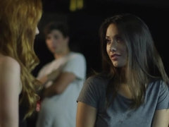 Two sexy women are in front of a crown in a bar, licking each other