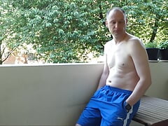 Man undressing outside on the balcony naked he wanks his semi-erect shaved cock becoming erect and gets dressed again